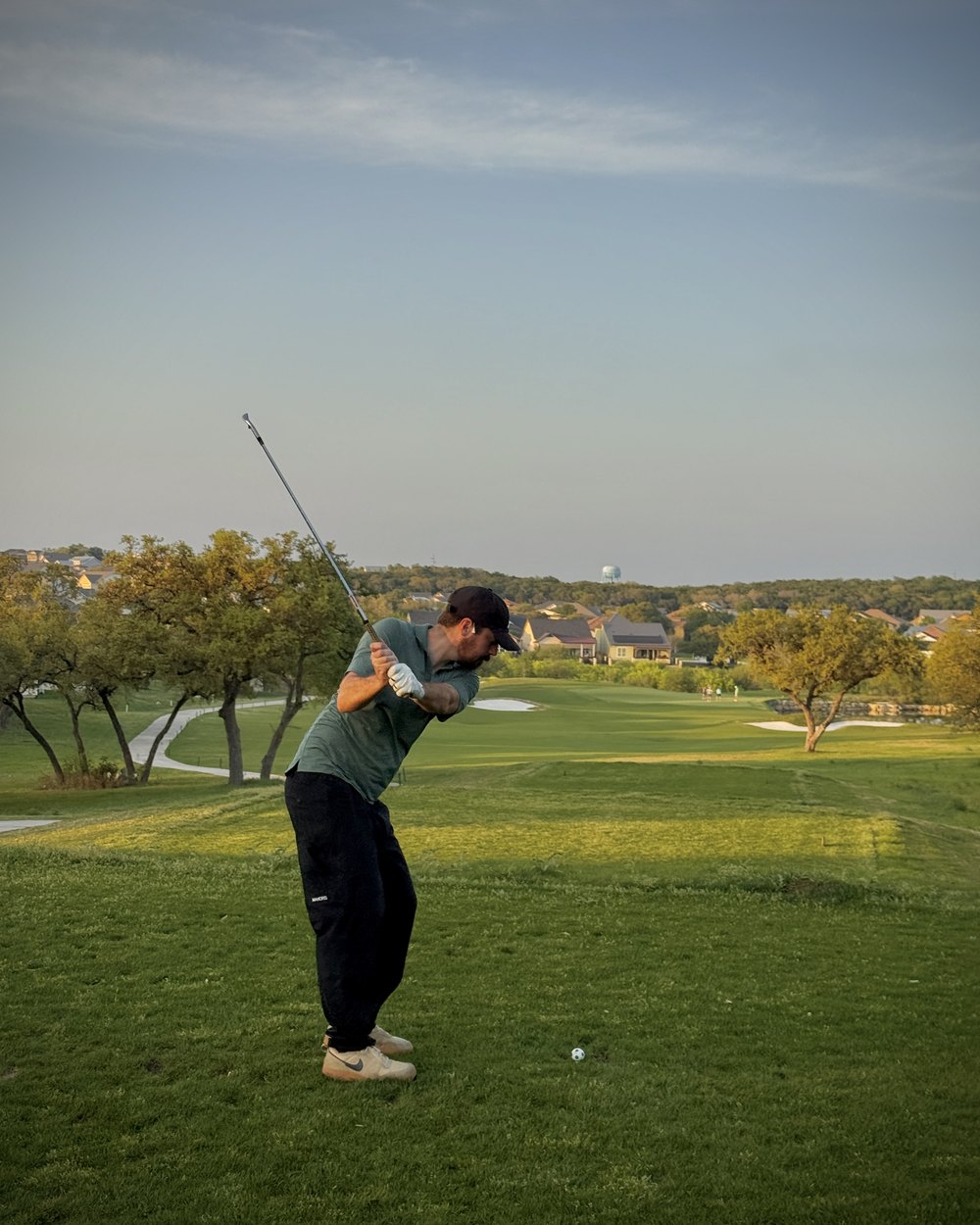 A golfer at the top of the backswing on an open Texas hole at dusk
