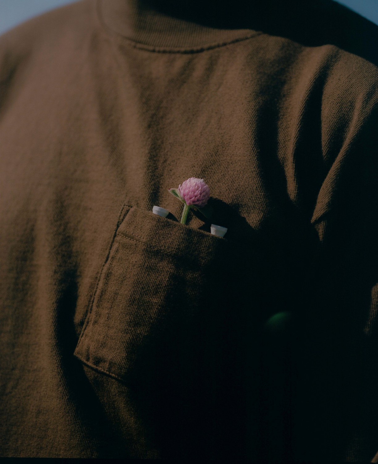 Close-up of the Work Shirt chest pocket holding two tees and a clover flower