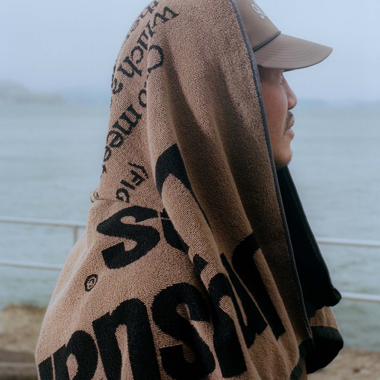 The Unusual Lies towel in Earth held up against the sea