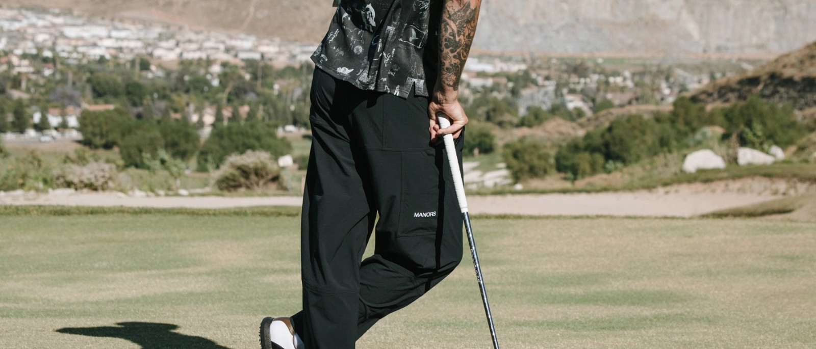 A golfer in black Manors trousers standing over a putt, from the Manors Golf lookbook