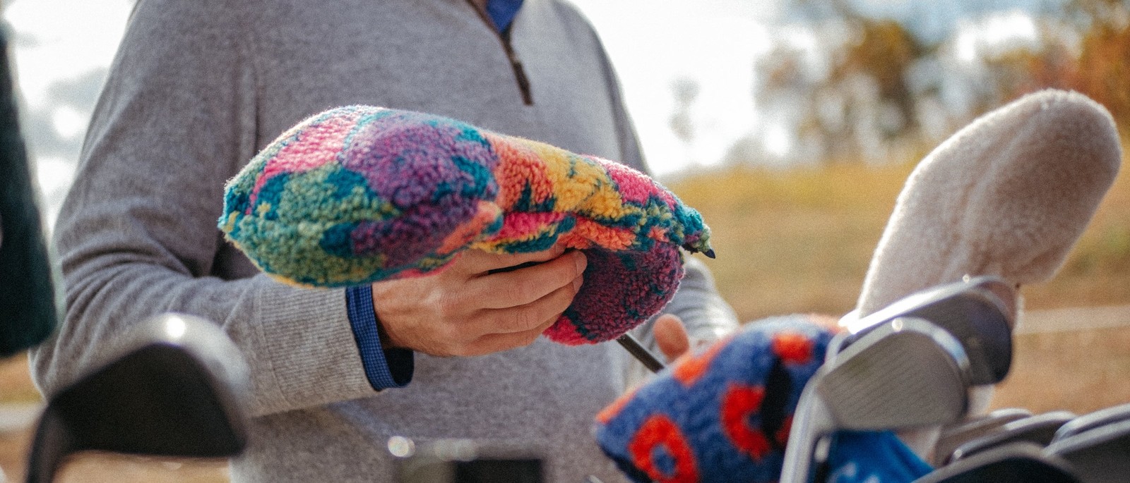 A tie-dyed Après Golf sherpa fleece headcover being lifted off a driver beside a golf bag