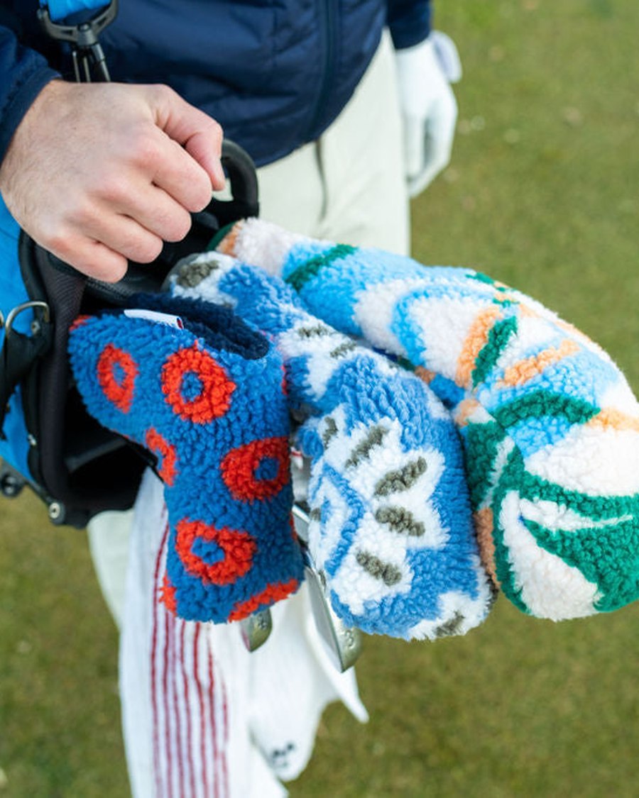 A hand lifting a printed Apr&egrave;s fleece cover off a driver in a stand bag, on course