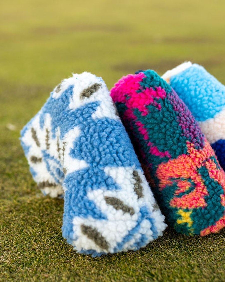 Three printed sherpa fleece headcovers lying on a cut green