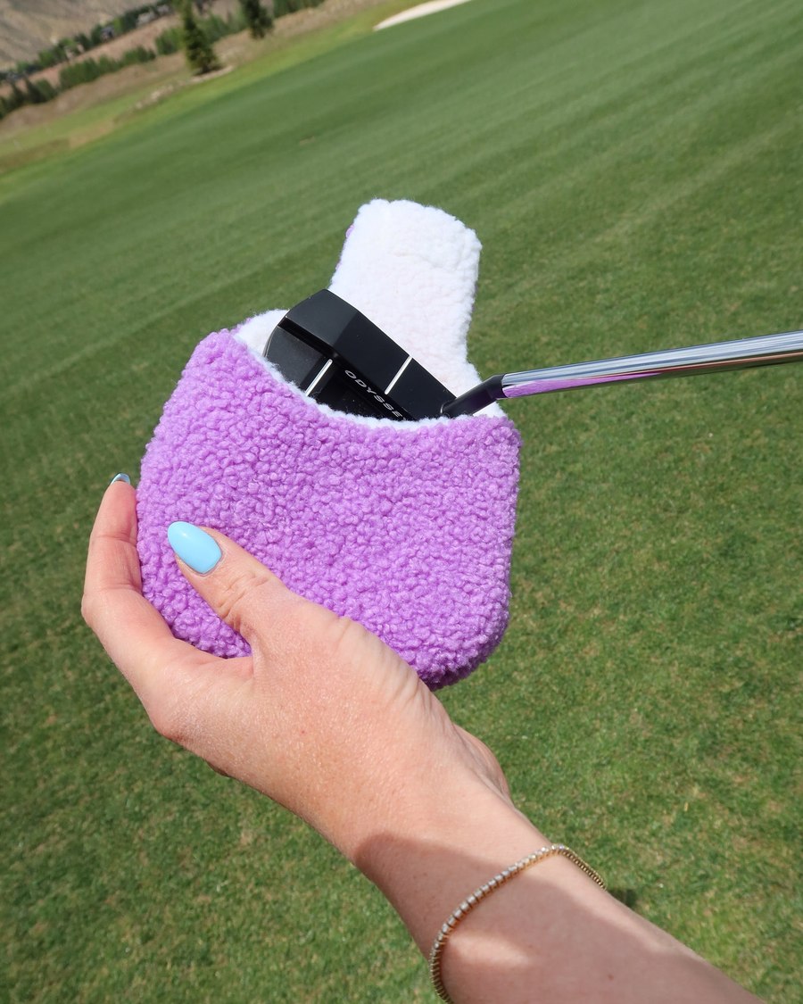 A lilac sherpa fleece cover held in one hand with the clubhead still seated inside