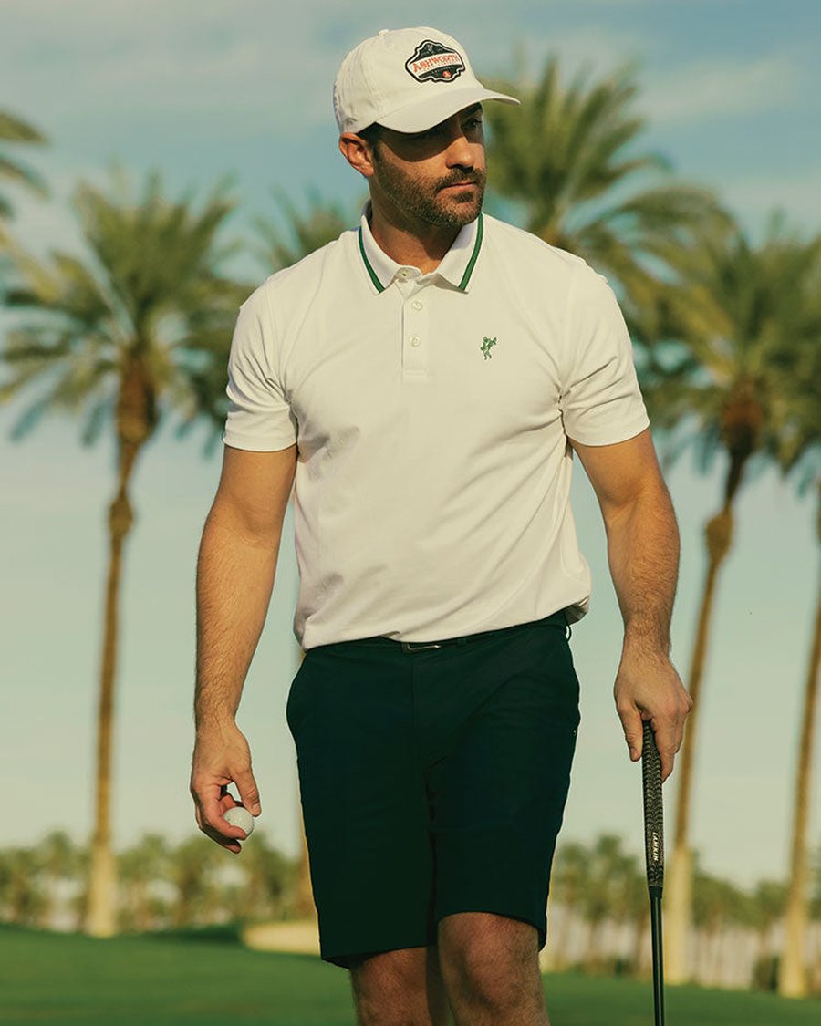 A golfer in a white Ashworth polo and green shorts among palms