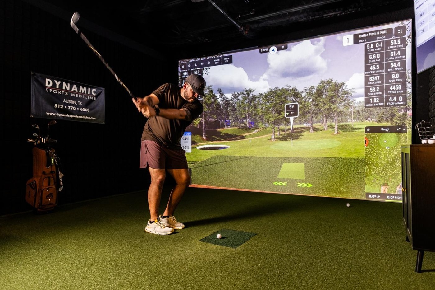 A golfer mid-swing in a simulator bay at 1872 Golf Club