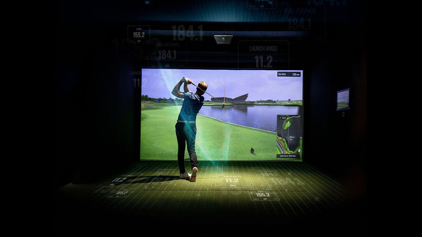 A golfer hitting into the screen in a darkened bay at ATX Indoor Golf Club