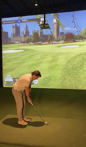 A golfer mid-swing in a bay at Fiber Golf