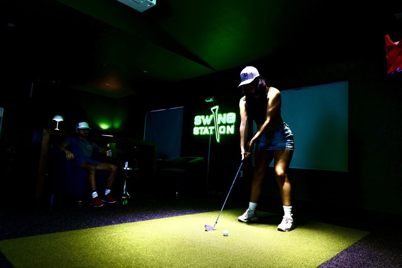 A golfer putting under the Swing Station sign in San Marcos