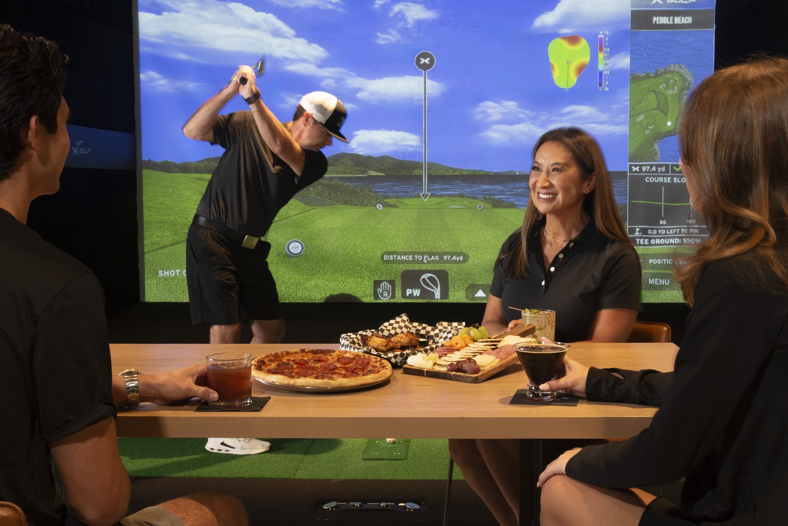 A group playing at X-Golf Cedar Park with food and drinks on the table
