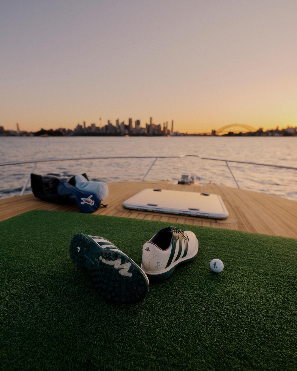 A Walker Golf Things bag and shoes on a turf mat at sunset by the water