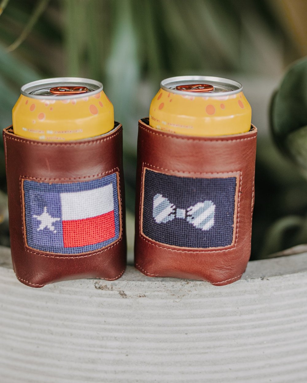 Two needlepoint can holders, one with the Texas flag, on a planter