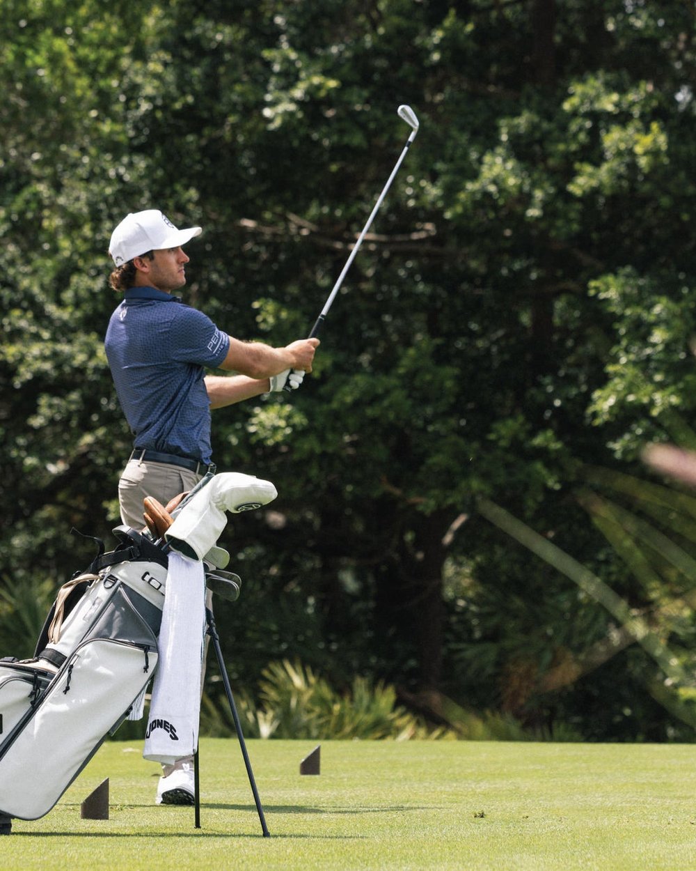 A golfer swinging beside a stand bag in long grass