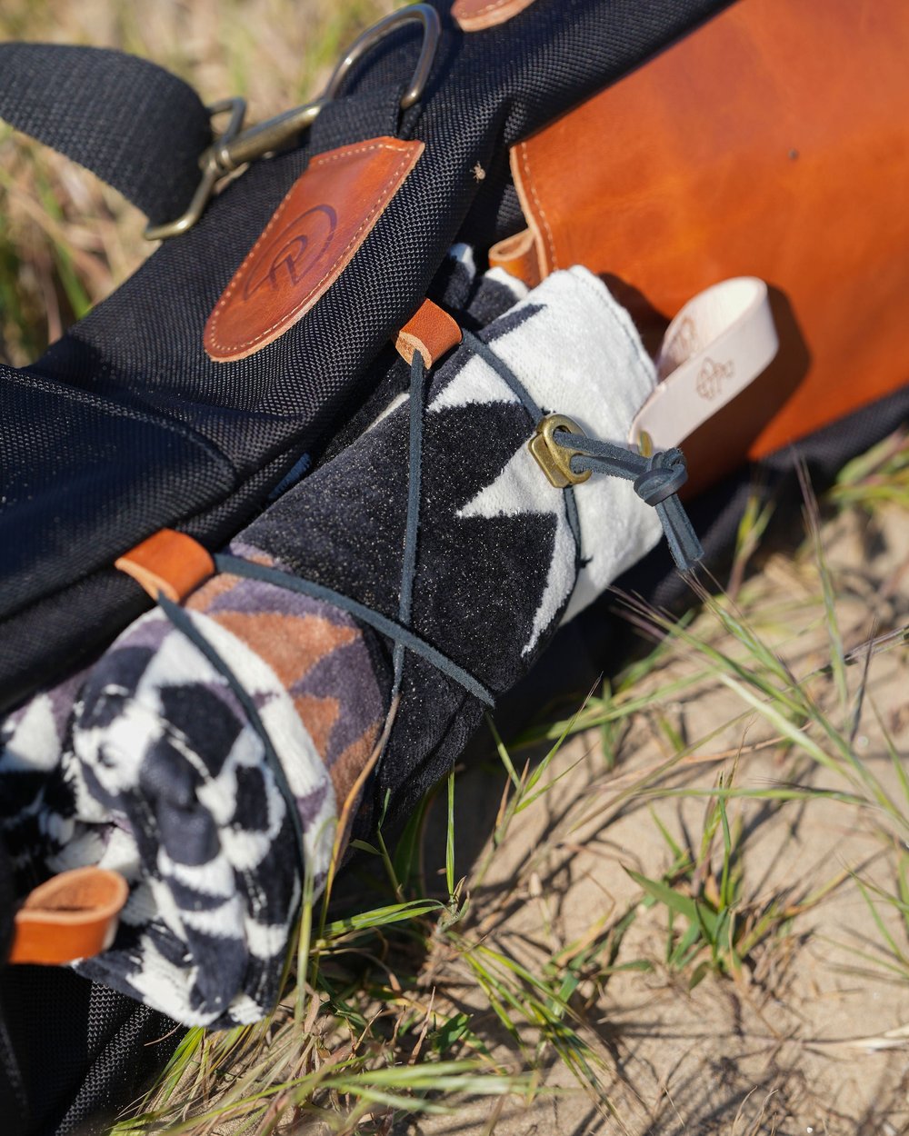 A black carry bag with a leather patch and a patterned headcover lying in tall grass