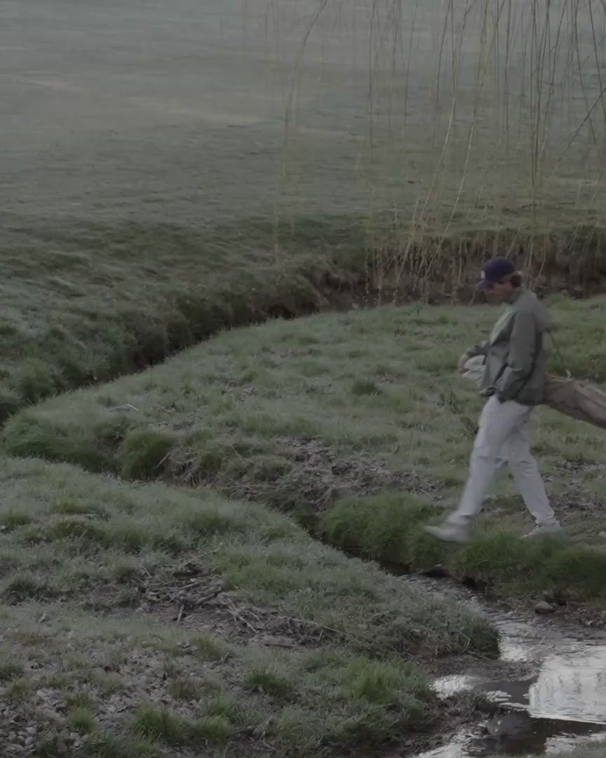 A golfer walking with his bag across a misty marsh