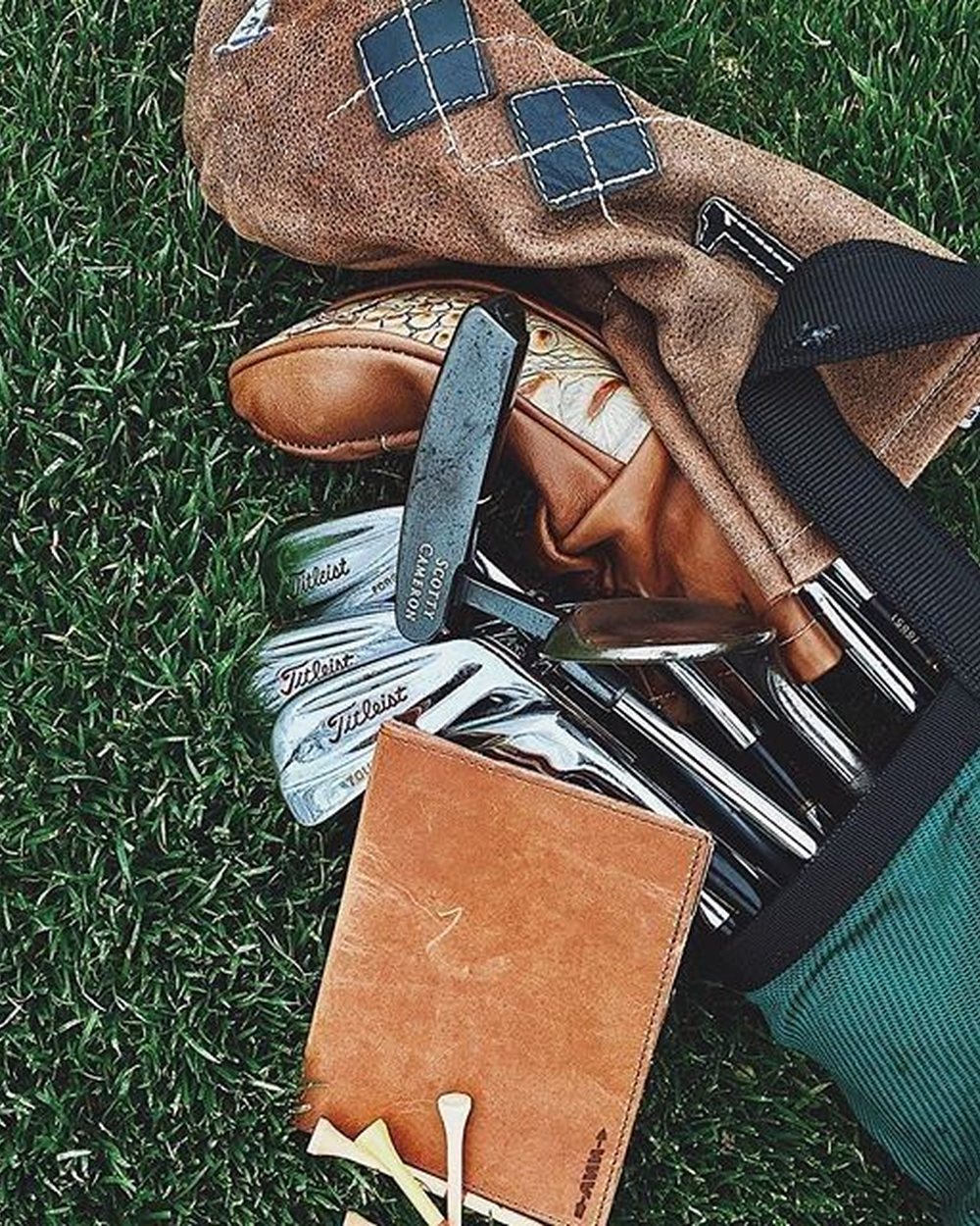 Via Pinterest photograph: A flat lay of irons, an argyle headcover and a tan leather wallet on grass