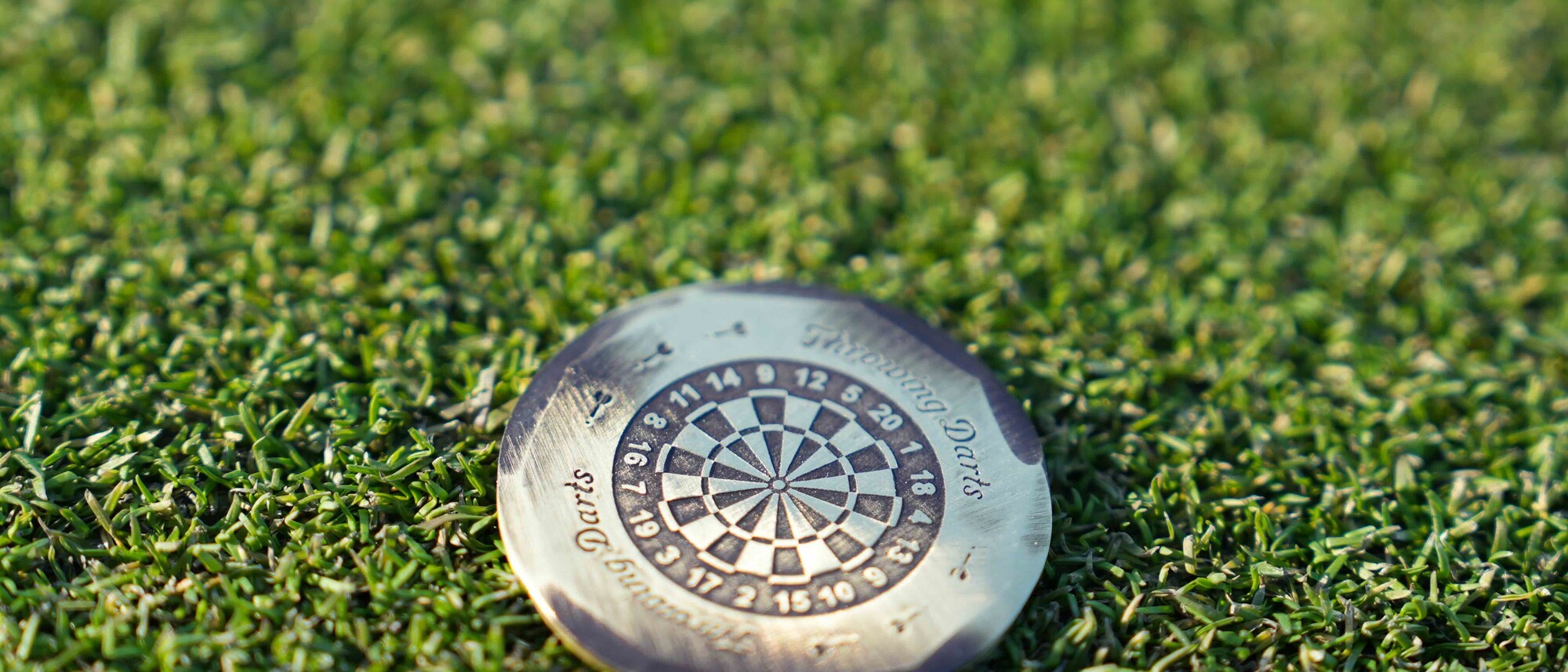 Seamus Golf hand forged Throwing Darts bronze ball marker resting on a putting green