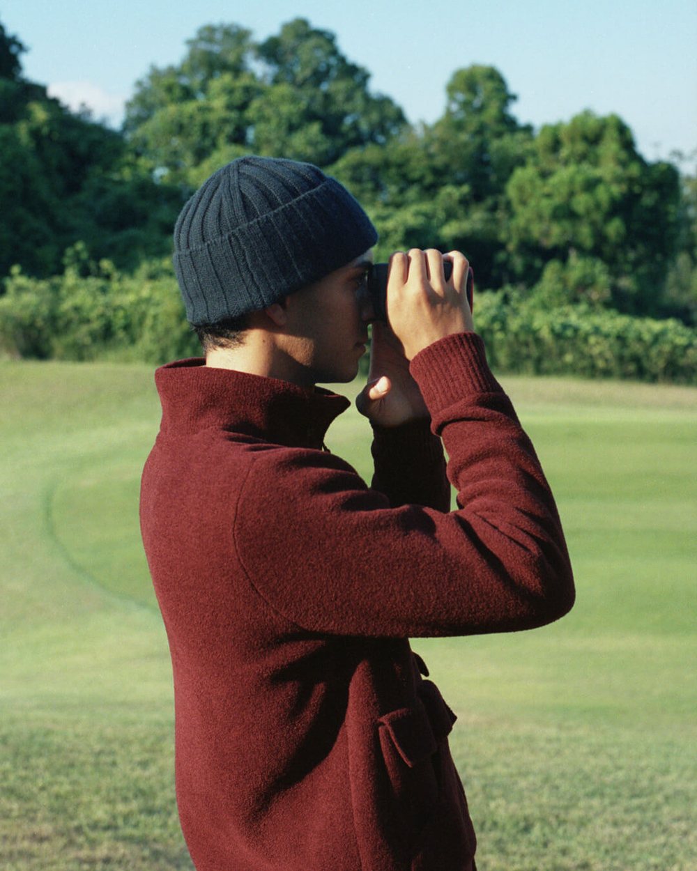 A man in a burgundy knit and a beanie checking a distance with a rangefinder on a fairway
