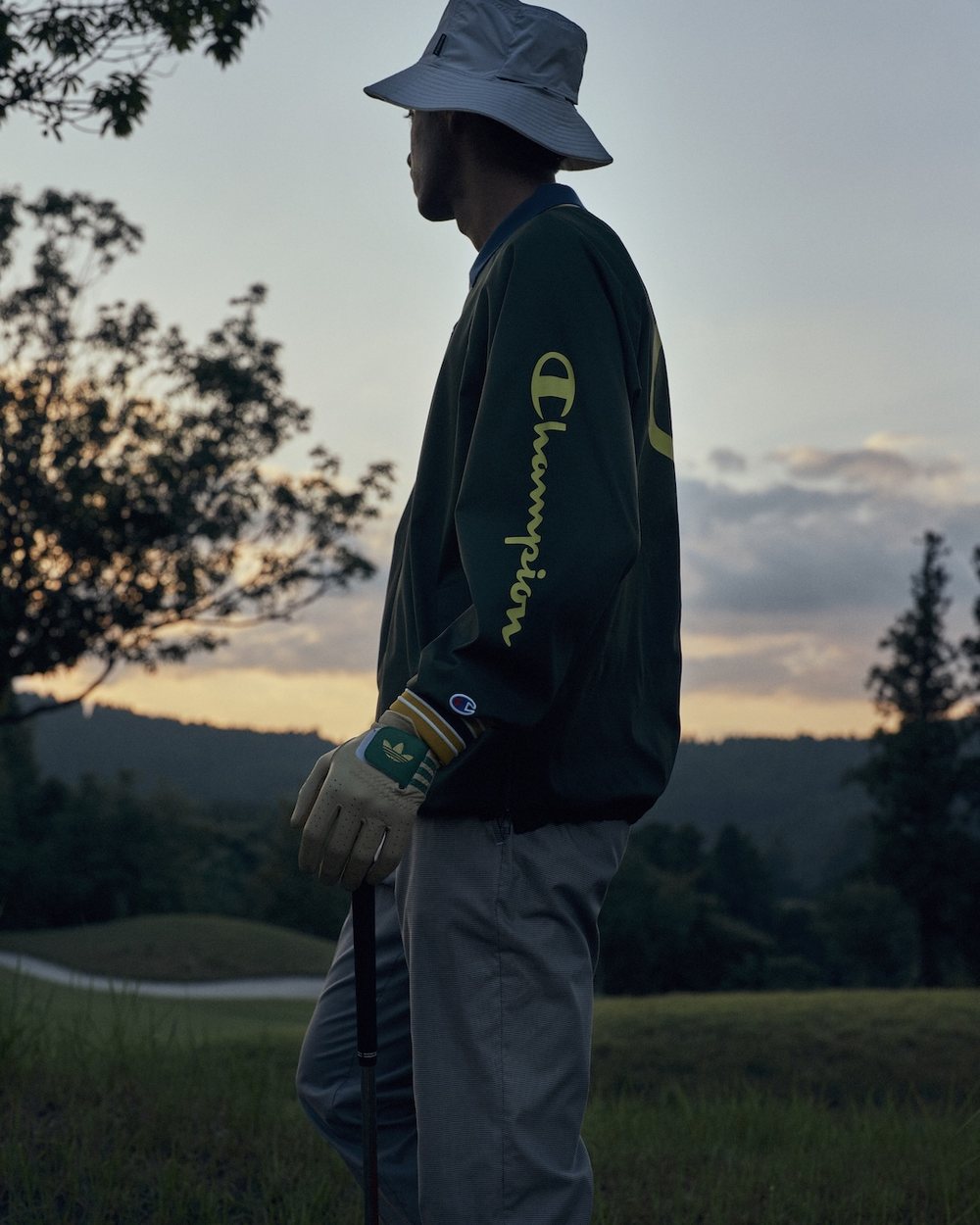 A golfer in a bucket hat and a green Champion jacket at dusk