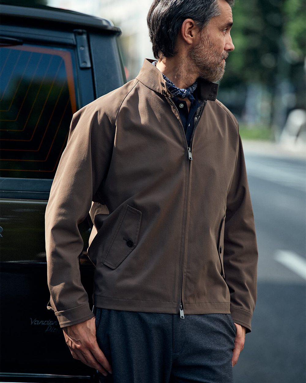 A man in a brown zip blouson standing by a car