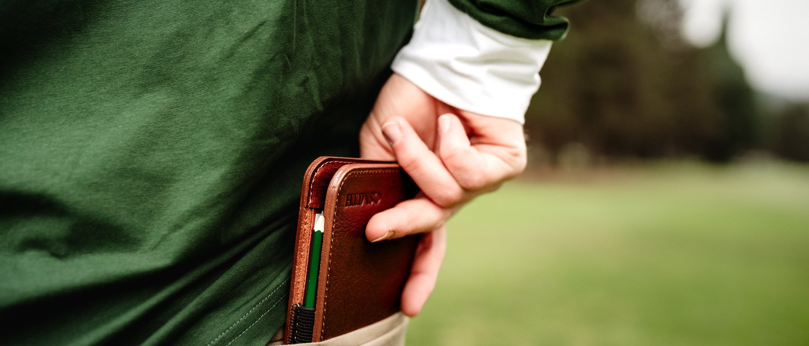 A hand pulling a Bluegrass Fairway Horween leather scorecard holder from a green jacket pocket on course