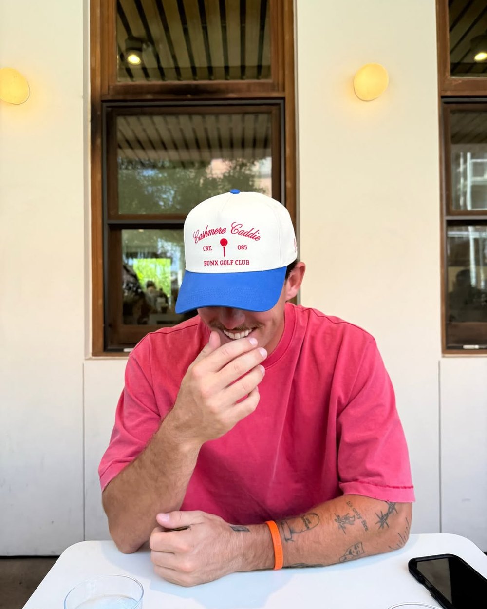 A man in a pink shirt and a Cashmere Caddie hat at a cafe table