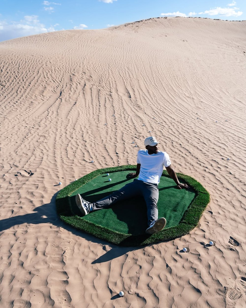 A golfer lying on a square of turf in the middle of sand dunes