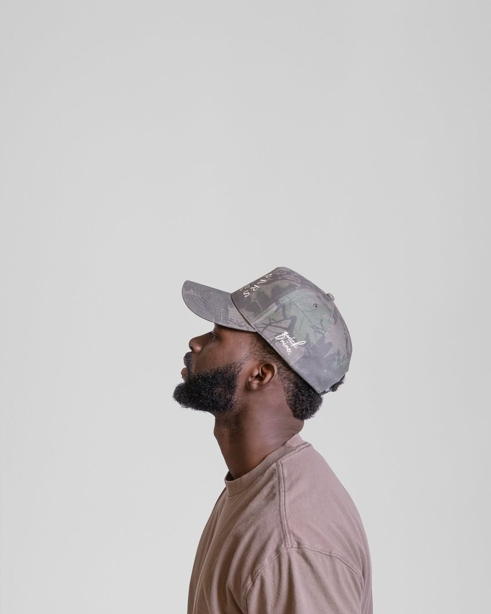 A man in a camo BUNX hat looking up against a gray wall