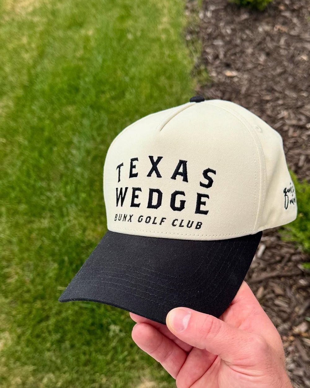 A hand holding the Texas Wedge hat over grass