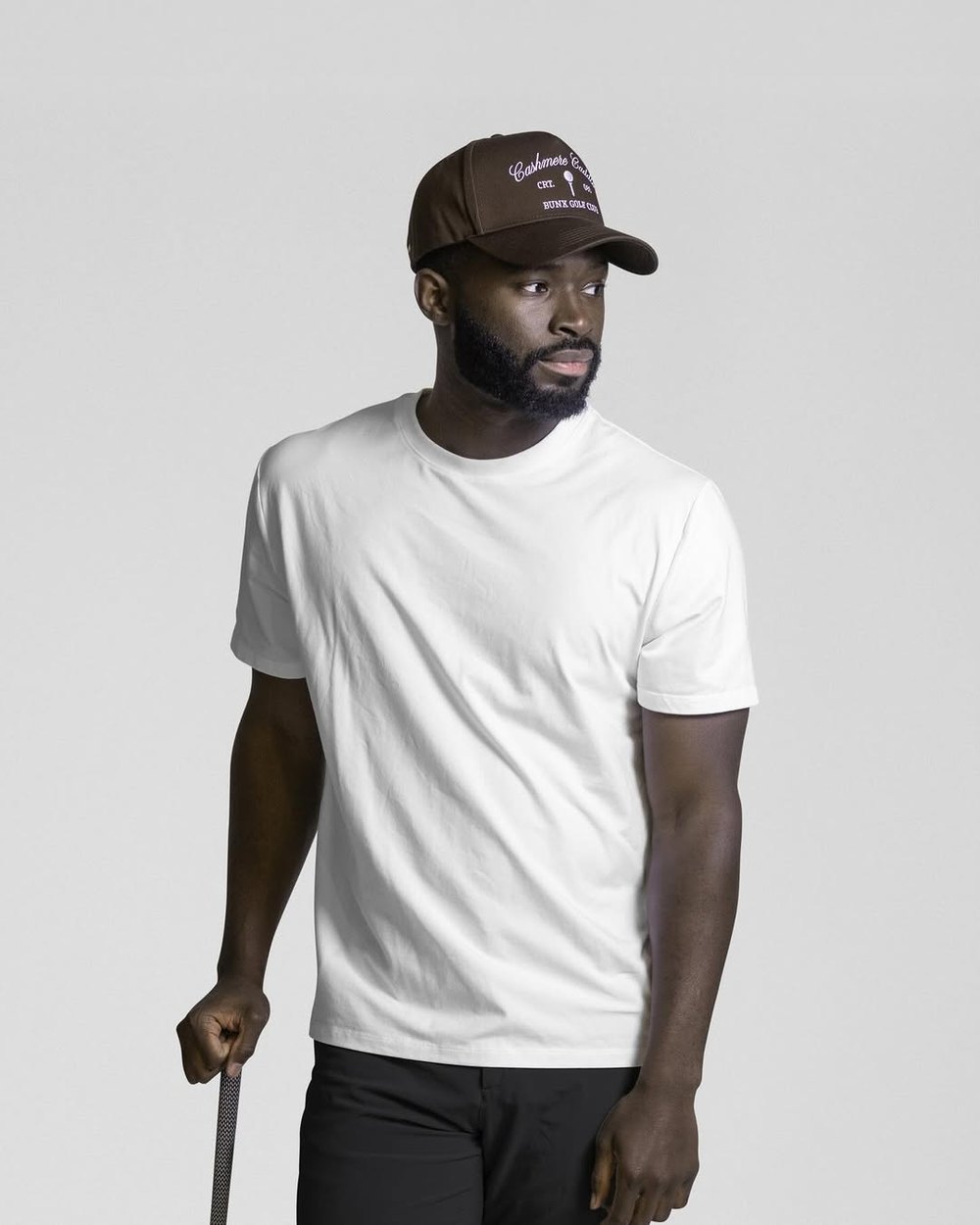 A man in a white T-shirt and a BUNX hat leaning on a club