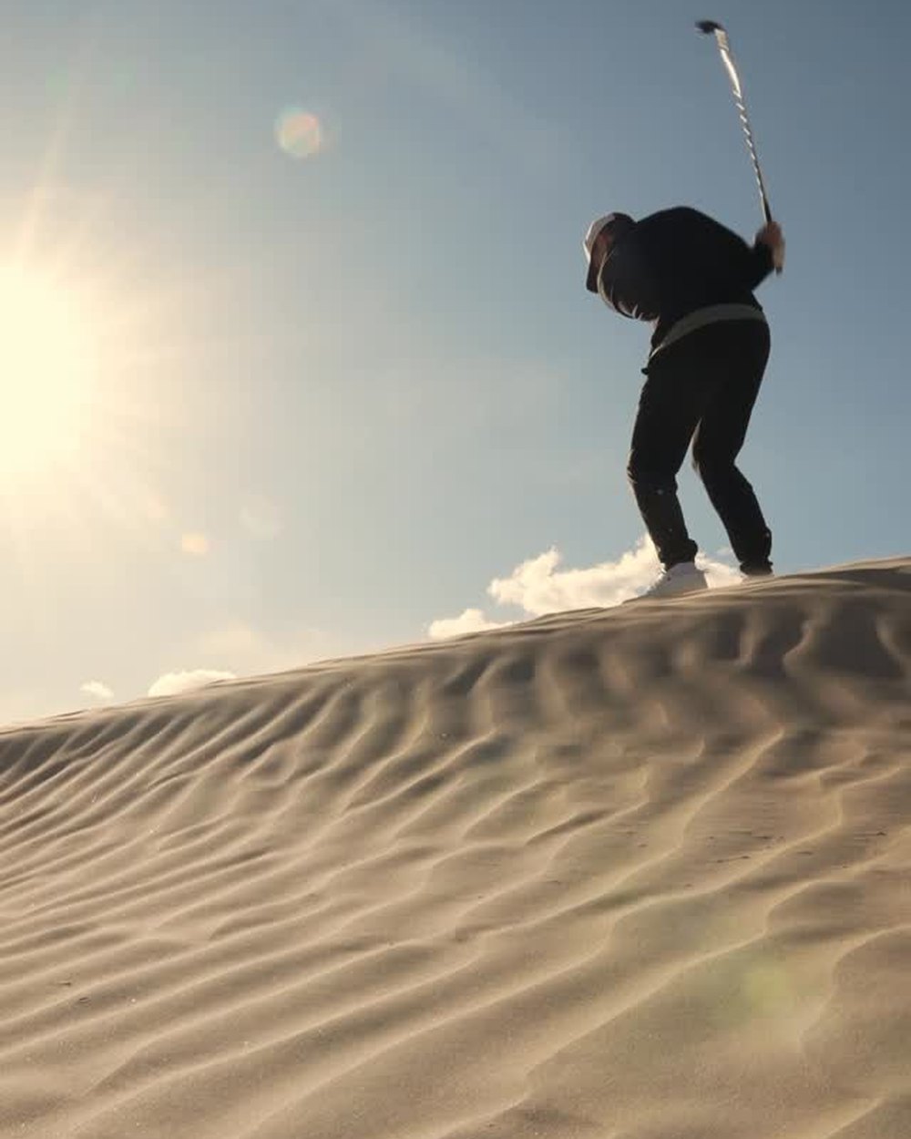 A golfer swinging at the top of a sand dune