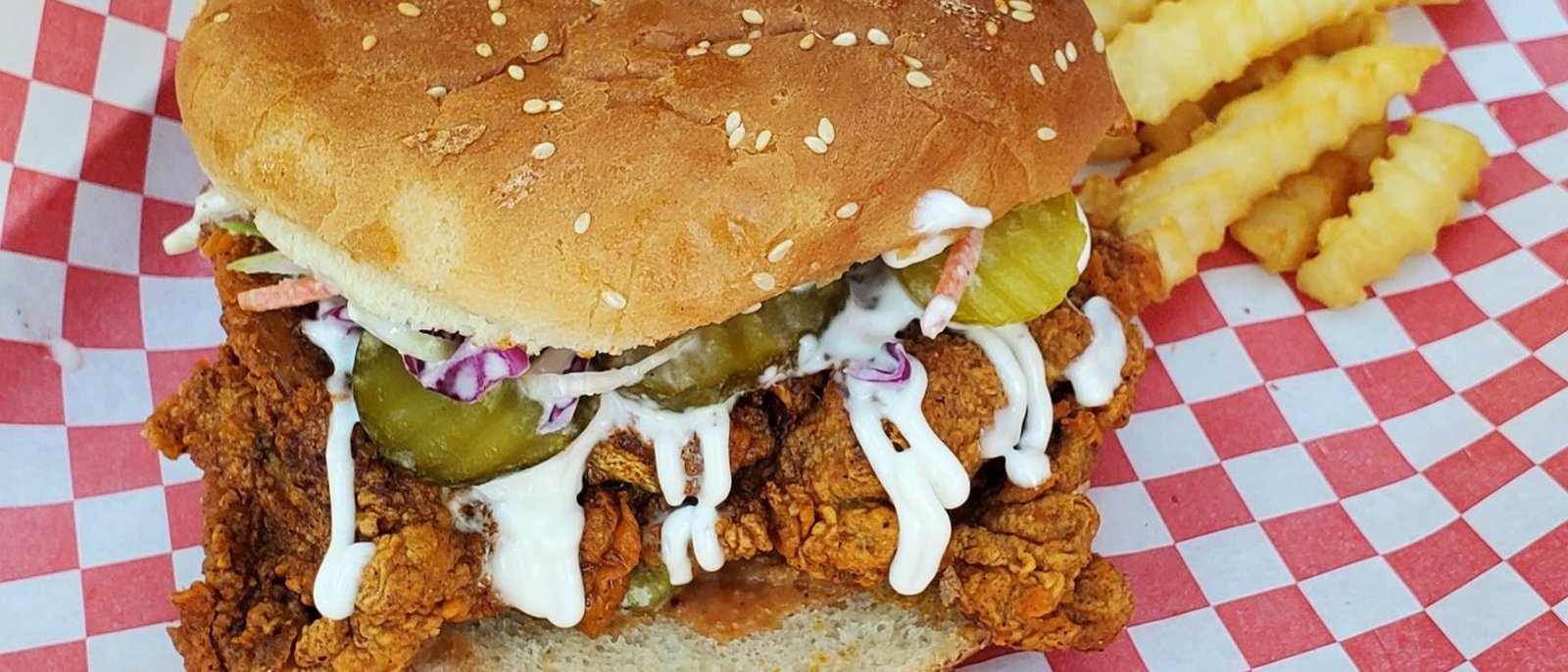 Dang Hot 89 fried chicken sandwich with pickles, slaw and sauce, crinkle fries on red-checked paper