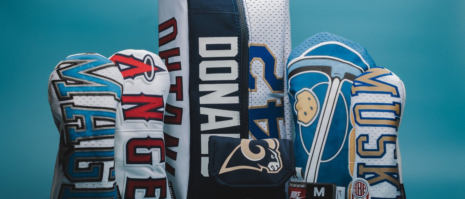 Clamp Golf Company headcovers cut from American football and sports jerseys, lined up against a blue backdrop