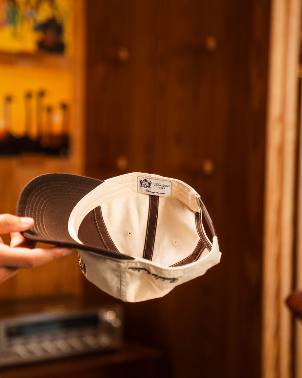 A hand holding a cream Woodgrain cap in a wood-paneled room