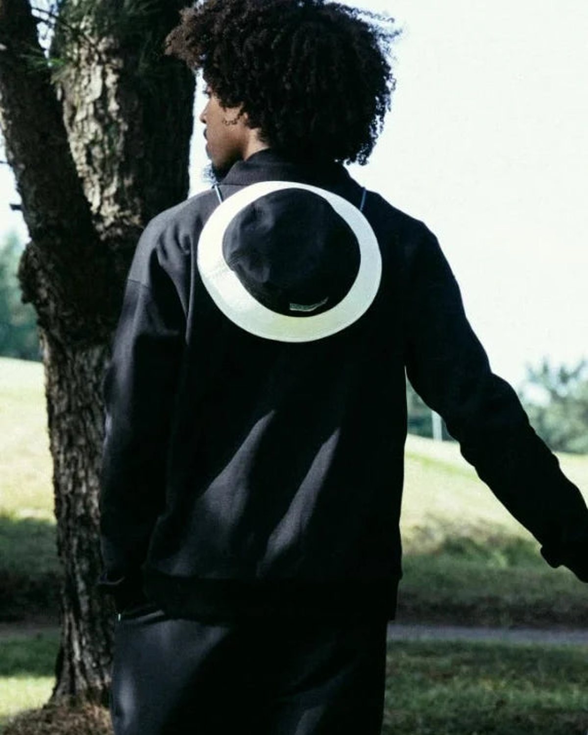 A player in a black outfit beside a pine tree, from Cph/Golf&rsquo;s lookbook for the Jones collaboration