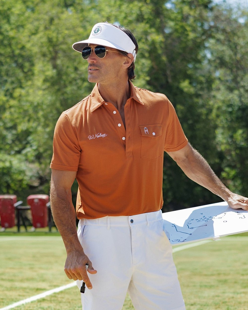 A golfer in the burnt-orange Coach Nelson Players Shirt and a white cap on a course