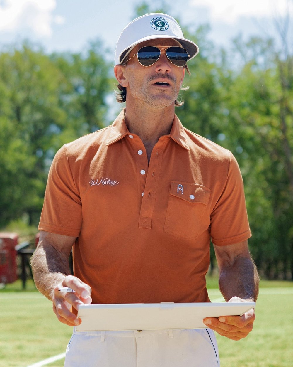 A golfer in Criquet's burnt-orange Coach Nelson Players Shirt