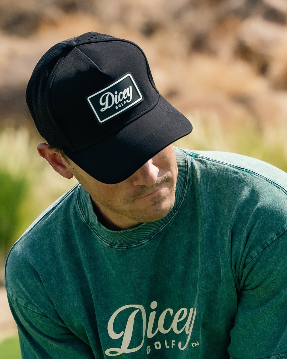 A man in a black Dicey hat and green sweatshirt in front of desert grasses