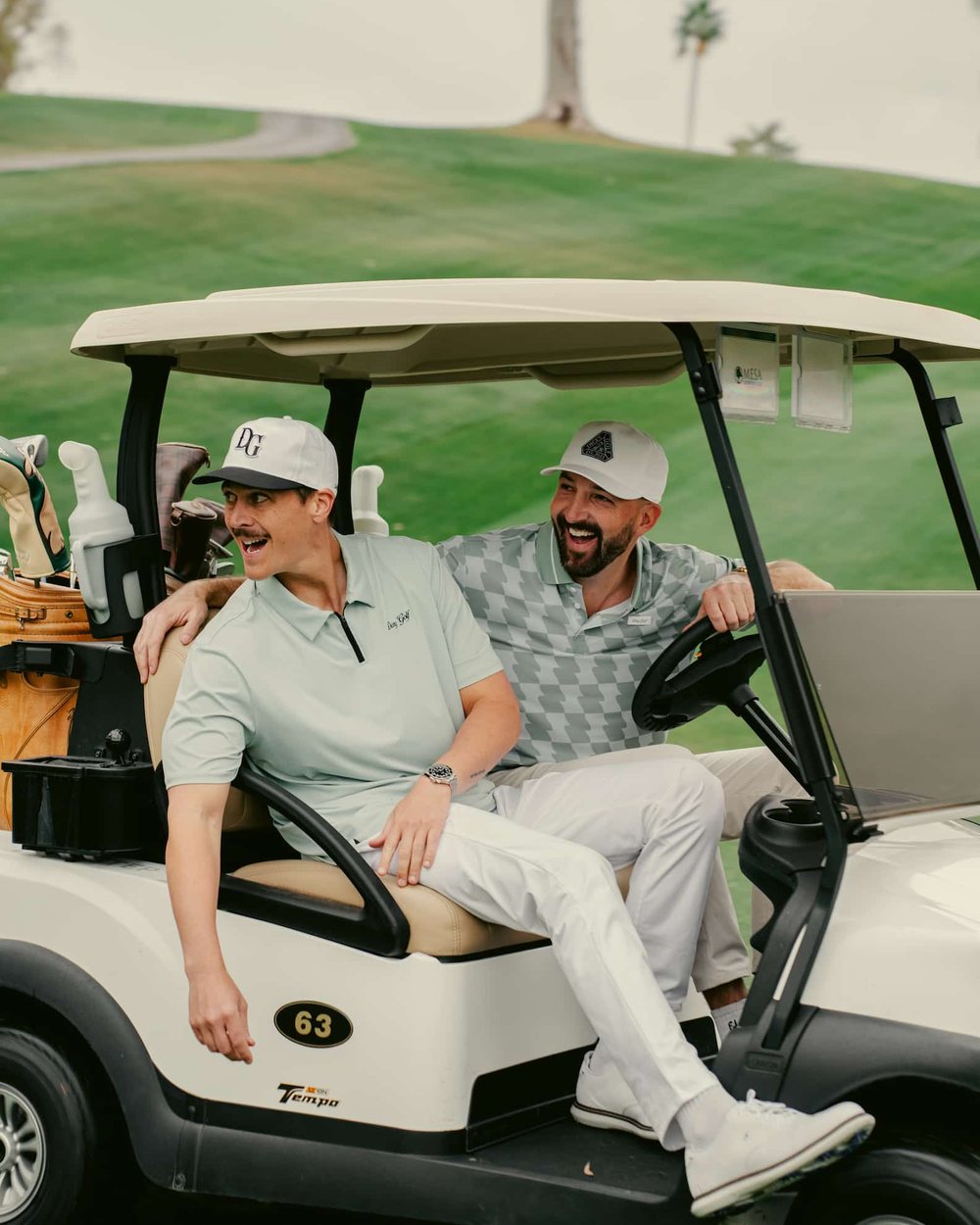 Two men laughing in a golf cart on a sunny course