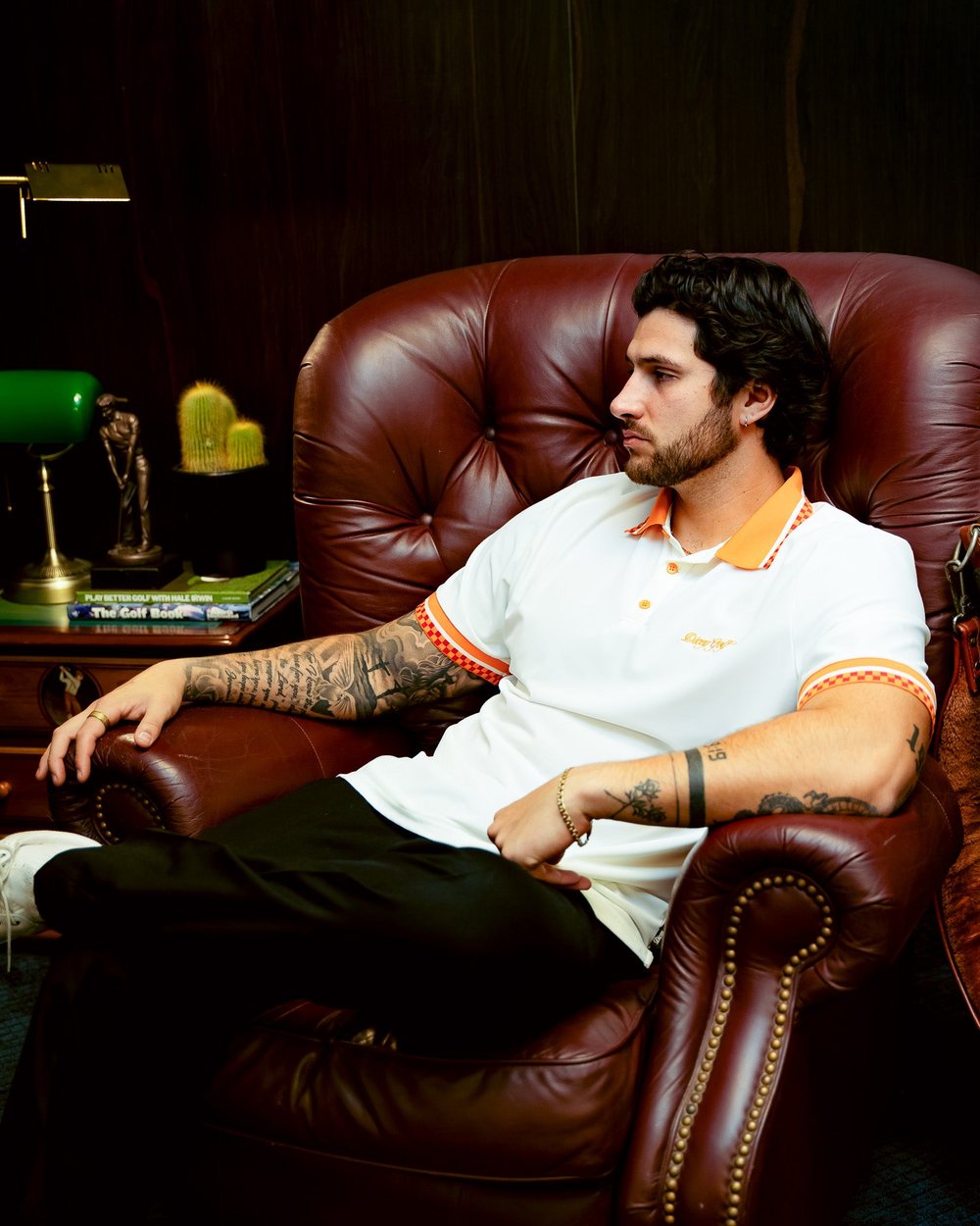 A man in a Dicey polo leaning back in a leather armchair in a wood-paneled room