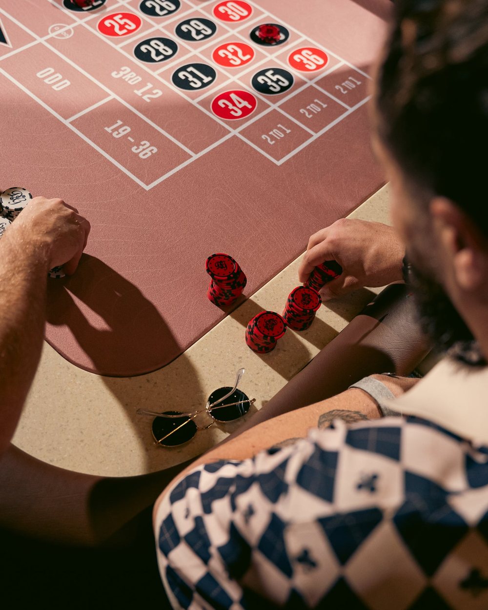 Two men placing chips on a roulette table, one in a checkered Dicey polo