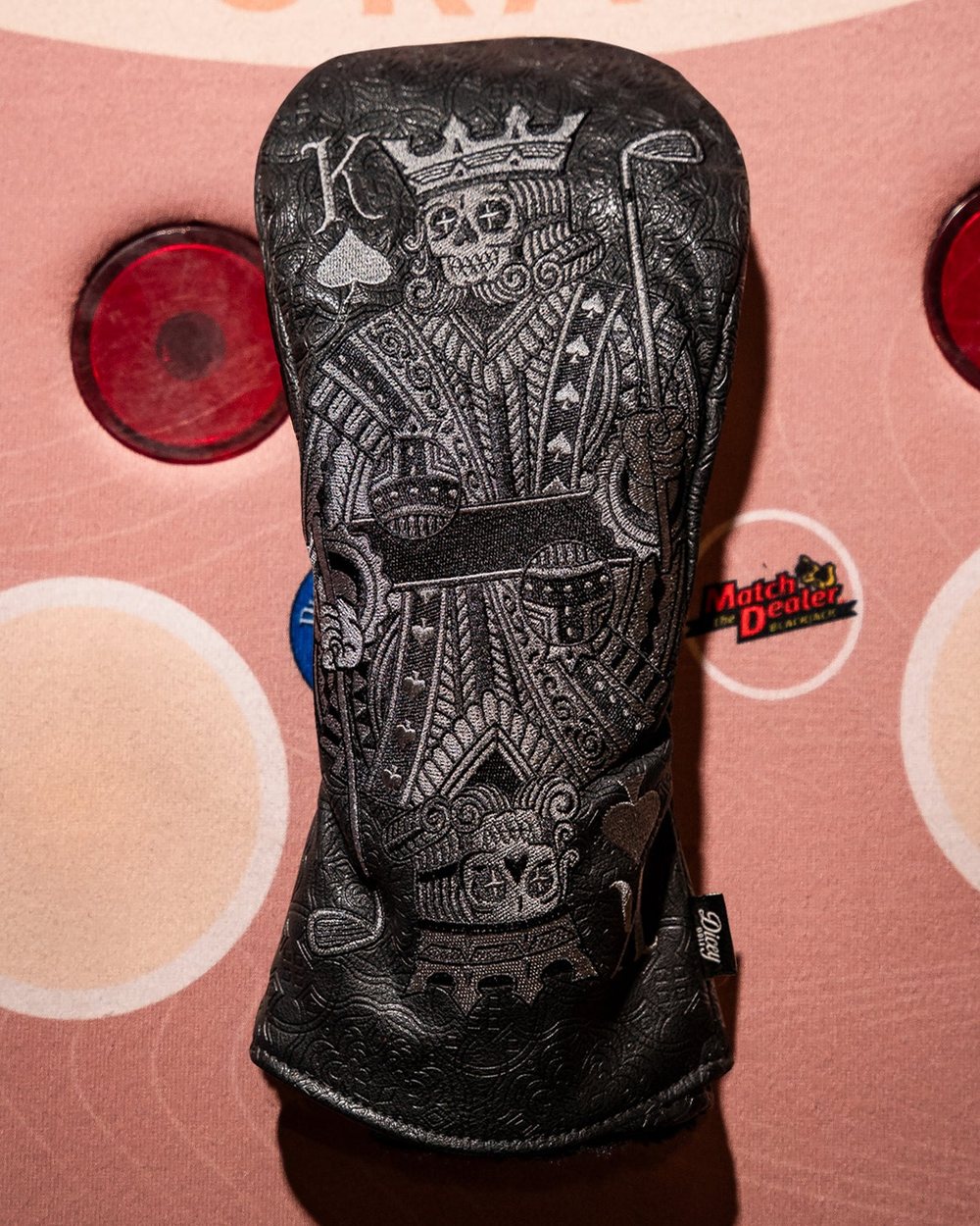 A black King of Spades headcover on a pink and red casino table