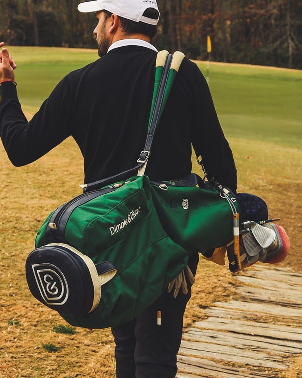 A golfer walking across a fairway with a green carry bag