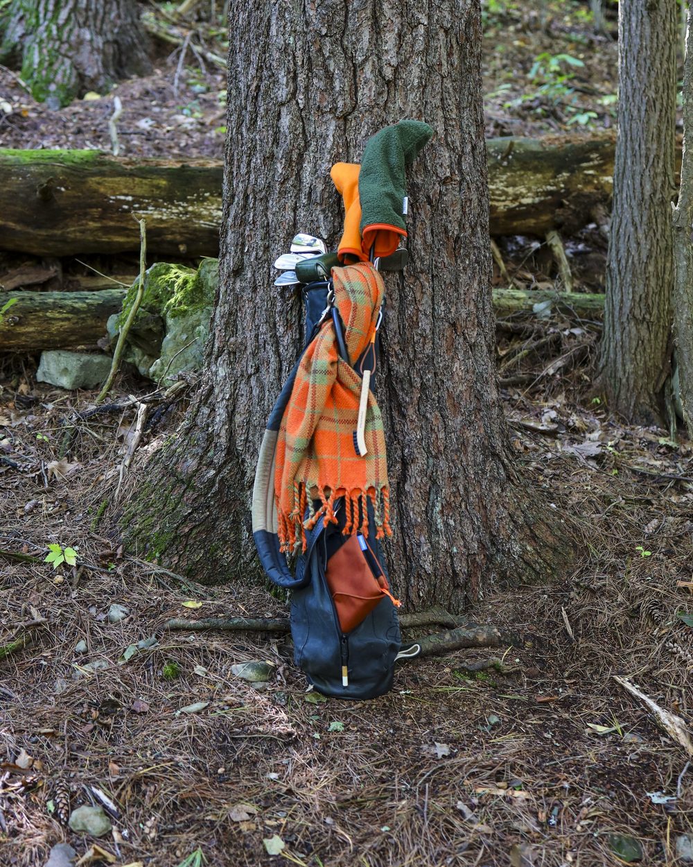 A golf bag with an orange fleece headcover propped against a tree in the woods