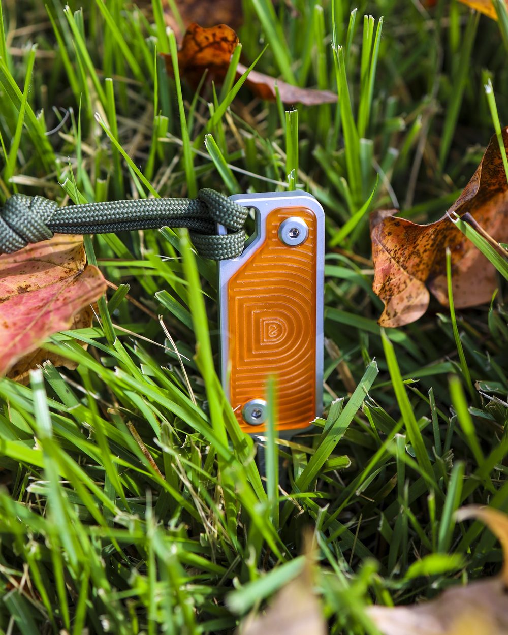 An orange aluminium divot tool in long grass and leaves