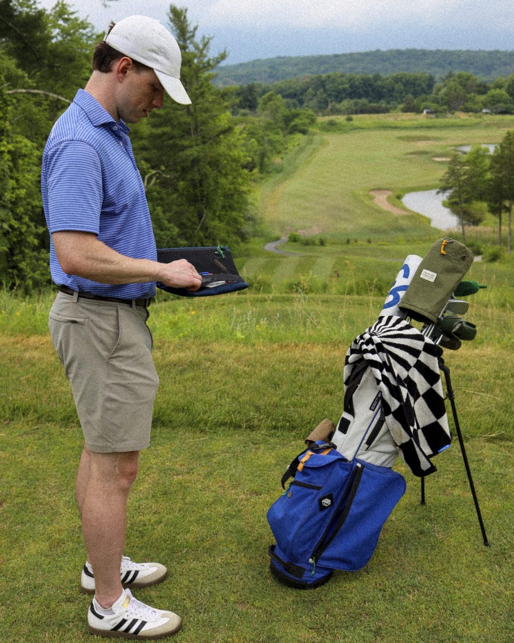A golfer standing beside a checked stand bag on the course