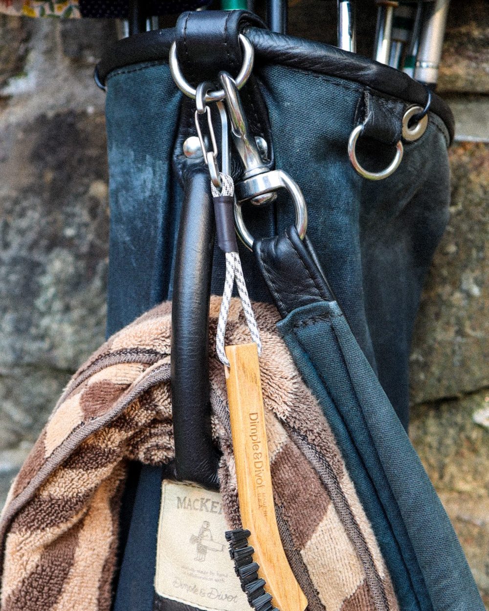 A hickory brush clipped to a golf bag beside a striped towel