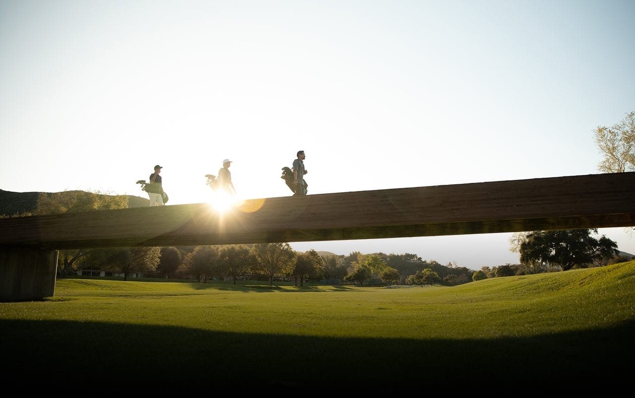 Golfers crossing a bridge on a golf course at sunrise, from STIX