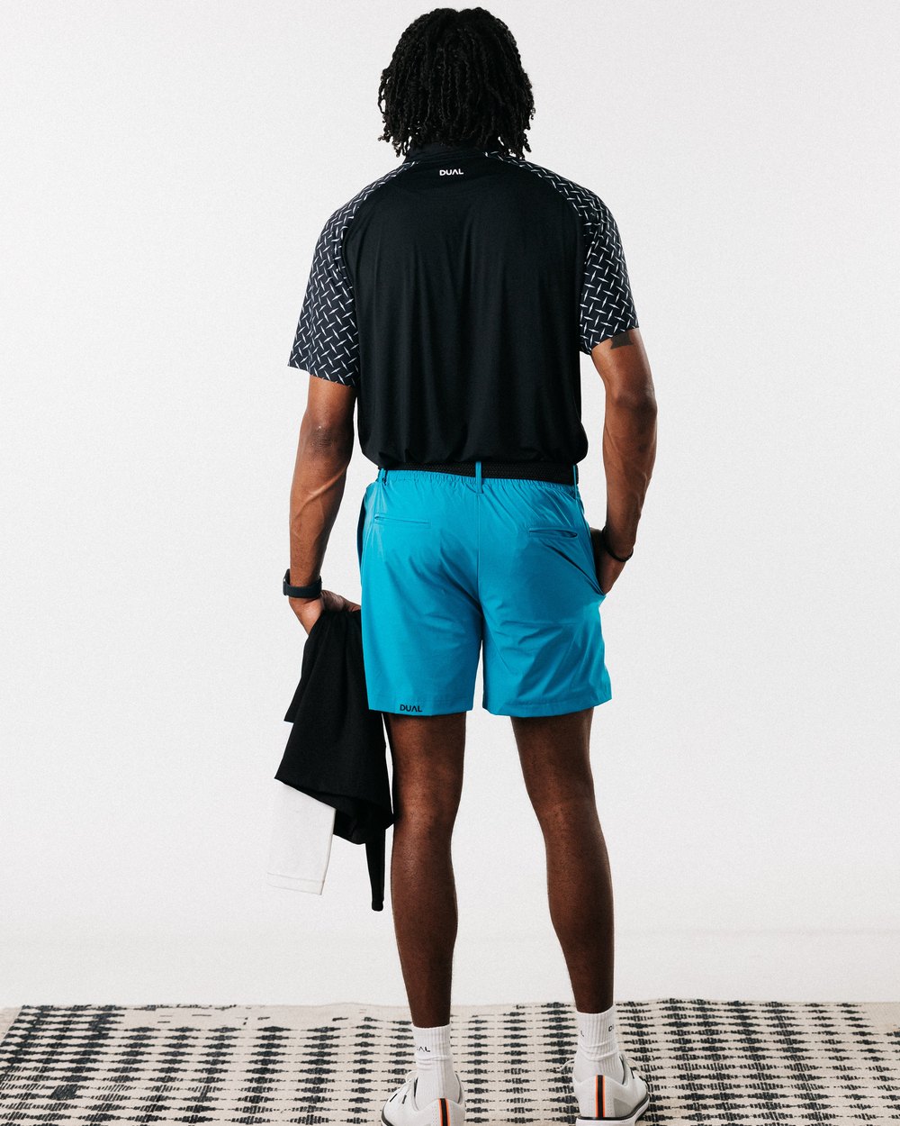 A man seen from behind in a black polo and electric blue Pursuit shorts
