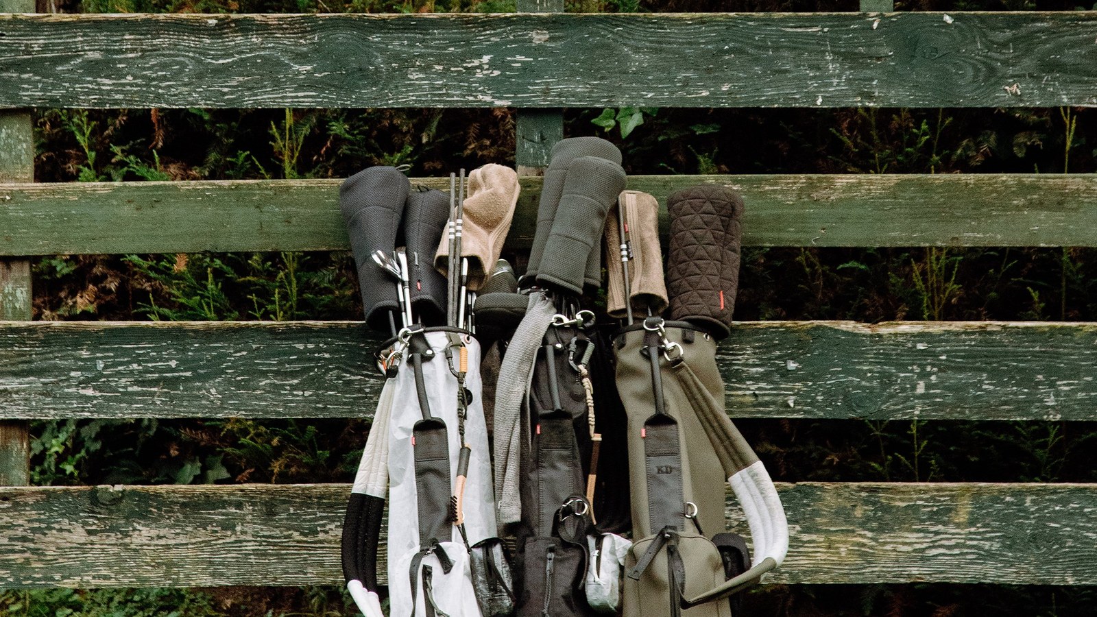 Three Sentinel Basecamp Walker golf bags in white and black Dyneema standing against a green bench